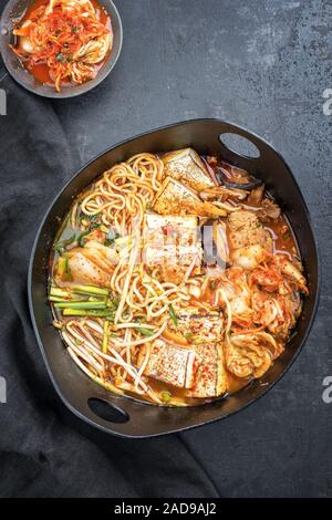 Traditionelles koreanisches Kimchi jjigae mit gegrillter Schweinebauch und Ramen als Draufsicht in modernem Design Japanische gusseiserne Rösten di Stockfoto