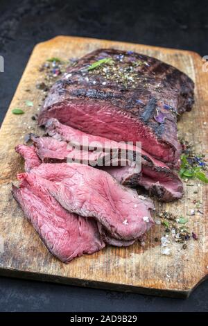 Traditionelle Grill trockenen Jahren in Scheiben Roastbeef Steak mit Kräuter als Closeup auf einem alten Schneidebrett Stockfoto