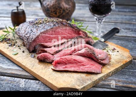 Traditionelle Grill trockenen Jahren in Scheiben Roastbeef Steak mit Kräuter als Closeup auf einem alten Schneidebrett Stockfoto