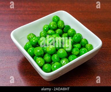 Nahaufnahme von frischen und feuchten grünen Erbsen in einer weißen Schüssel auf einen hölzernen Tisch. Stockfoto