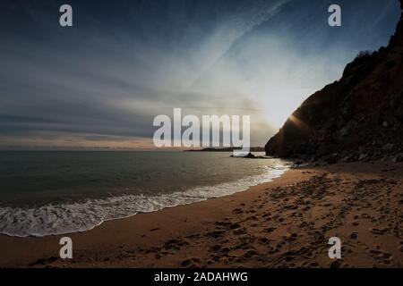 Die Sonne schön hinter den Klippen von St. Austell, Cornwall, England. Die Leute haben bereits den Strand verlassen. Stockfoto