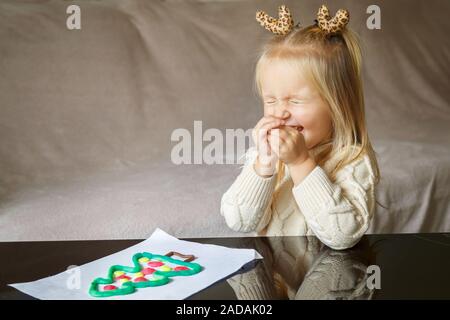 Adorable kleine Mädchen mit blonden Haaren spielen mit Lehm und Weihnachtsbaum zu Hause Stockfoto