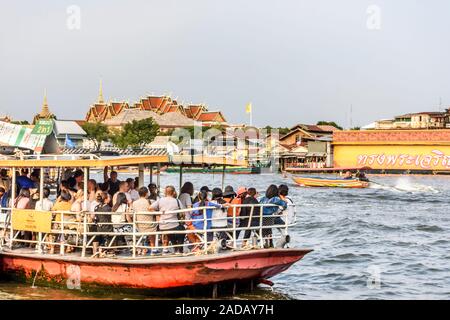 Bangkok, Thailand - 17. November 2019: River Taxi nimmt Fahrgäste am Wat Arun am Chao Phraya Fluss mit Wat Pho hinter Stockfoto