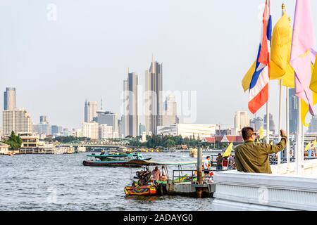 Bangkok, Thailand - 17. November 2019: Touristische außerhalb Wat Arun nimmt selfie von Chao Phraya River, mit Skyline von Bangkok hinter Stockfoto