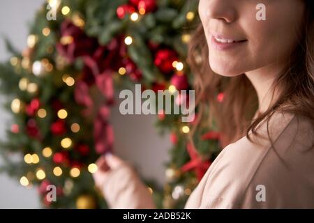 Schöne festliche Kranz aus frischem Fichte in der Frau die Hände. Xmas Stirnreif mit roten und goldenen Verzierungen und Bälle. Weihnachtliche Stimmung. Graue Wand im Hintergrund. Stockfoto