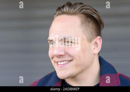 Hübscher junger Mann beiseite, mit einem Lächeln der Freude in einer Nahaufnahme Kopf schoss auf eine graue Wand Stockfoto