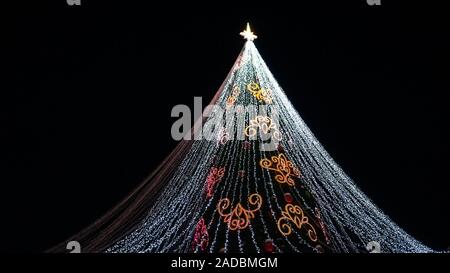 Oben auf der künstlichen Weihnachtsbaum von Golden beleuchtete LED-Lichter gegen den dunklen Nachthimmel. Winterurlaub. Stockfoto