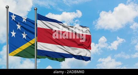 Salomonen und Costa Rica Flagge im Wind gegen Weiße bewölkt blauer Himmel zusammen. Diplomatie Konzept, internationale Beziehungen. Stockfoto