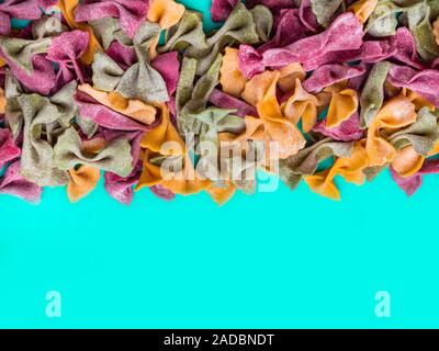 Stapel der Italienischen getrocknet, Dreifarbig Farfalle Pasta. Verschiedene Farben von Bow Tie auf blau Farbe Hintergrund Stockfoto