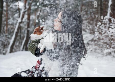 Es ist Schneefall. Smiling brunette Spaß beim Spaziergang mit ihrem Hund im Winter Park Stockfoto