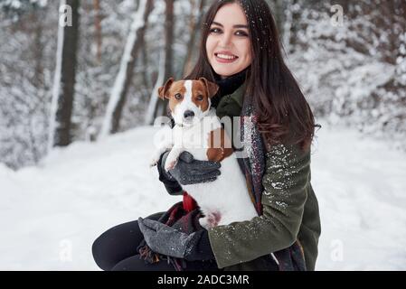 Pet in den Händen hält. Smiling brunette Spaß beim Spaziergang mit ihrem Hund im Winter Park Stockfoto