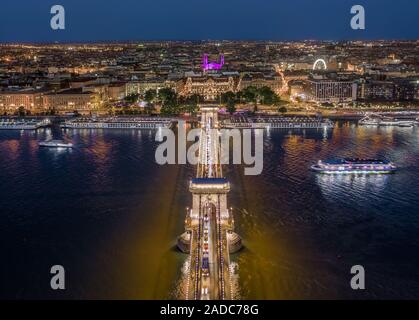 Budapest, Ungarn - Luftaufnahme von beleuchteten Széchenyi Kettenbrücke mit St.-Stephans-Basilika, Riesenrad und Kreuzfahrtschiffe auf dem Fluss Donau bei Bl Stockfoto