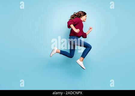 Volle Länge Körper Größe Foto von Lockig wellig Fröhliche trendigen Jugendlichen in Jeans Denim burgund Pullover laufen Springen in Richtung Shopping Mall isoliert Stockfoto