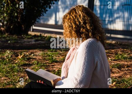 Blonde und lockig behaarte Frau liest im Park Stockfoto