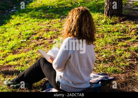 Blonde und lockig behaarte Frau liest im Park Stockfoto