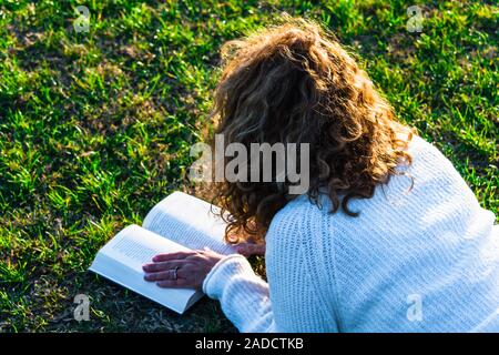 Blonde und lockig behaarte Frau liest im Park Stockfoto