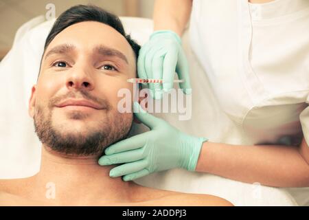Junge lächelnde Mann, Hyaluronsäure Einspritzanlage Stockfoto