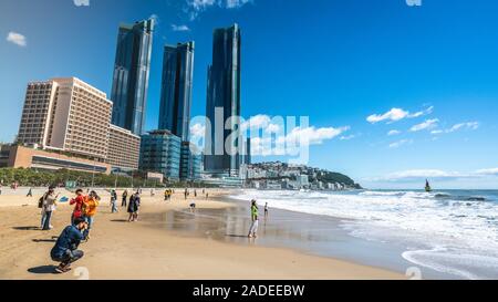 Busan, Korea, 3. Oktober 2019: asiatische Touristen auf Haeundae Beach an sonnigen Herbsttag und moderne Stadt Wolkenkratzer von Haeundae LCT Die scharfen im Hintergrund Stockfoto