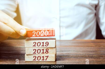 Geschäftsmann baut Holzklötze 2020. Das Konzept der Anfang des neuen Jahres. Neue Ziele. Nächste Jahrzehnt. Trends und Veränderungen in der Welt. Bauen pl Stockfoto