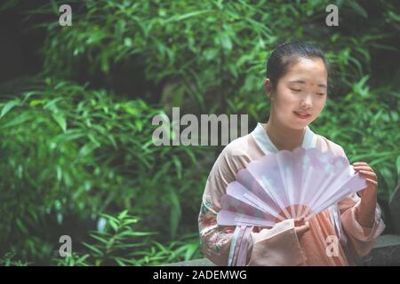 Chengdu, China - Juli 2019: Porträt einer jungen asiatischen chinesischen Braut, einen Fächer in der Trauung im Park Stockfoto