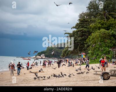 Batu Ferringhi Beach, Malaysia - November 2019: Tauben und Touristen in weißen sandigen Küste Boote und Jetskis bewölkten Tag im asiatischen Inseln Stockfoto