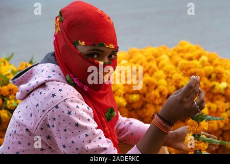 UDAIPUR, INDIEN - 27. OKTOBER 2018: Frau das Tragen der roten Islamischen hijab liegt neben der Tagetes, Girlanden am 17. Oktober 2019 in Udaipur, Raja zu Stapeln Stockfoto