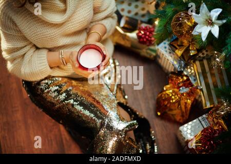 Nahaufnahme auf trendige mittleren Alter Hausfrau in Gold Pailletten Rock und weißen Pullover unter dem geschmückten Weihnachtsbaum in der Nähe des heutigen Boxen holding Tasse Milch. Stockfoto