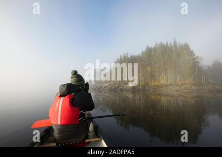 Kanufahren auf dem Loch Beinn a' Mheadhoin mit Gemeine Kiefer (Pinus sylvestris) Wald im Nebel bei Sonnenaufgang, Glen Affric, Highlands, Schottland. Stockfoto