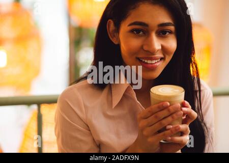 Dunkelhaarige Frau mit Latte lächelnd in die Kamera Stockfoto