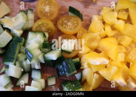 Gehackte gelbe mini Tomaten, gelbe Paprika und Gurke auf einem Schneidebrett. Ein Schritt der Erstellung selbstgemachten Salat für Tortillas. Stockfoto