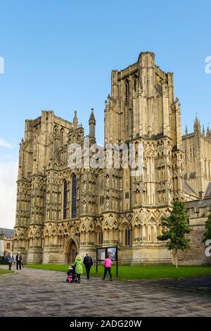 Wells Cathedral West Front mit Menschen zu Fuß hinter dem Hinweisschild. Kathedrale Grün, Brunnen, Mendip, Somerset, England, Großbritannien, Großbritannien Stockfoto