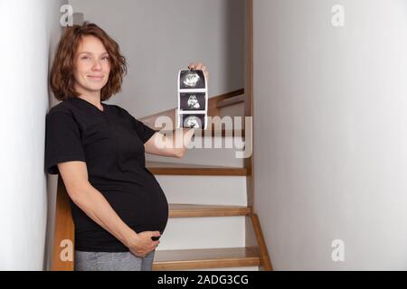 Schwangere curly Frau ihr Baby Sonographie. Glücklich werdende Dame genießen erste Foto von ihrem ungeborenen Kind, ihr zukünftiges Leben zu antizipieren, kopieren Stockfoto