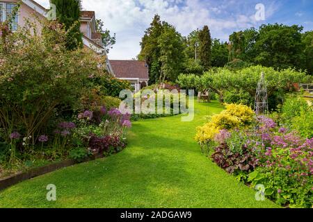 Blick auf abfallenden Garten mit Wicklung Blumenrabatten. Mit Euonymus undulata 'Emerald'n Gold', Alliums, Heuchera 'Hadspen Blood' und Phuopsi Stockfoto