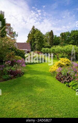 Blick auf abfallenden Garten mit Wicklung Blumenrabatten. Mit Euonymus undulata 'Emerald'n Gold', Alliums, Heuchera 'Hadspen Blood' und Phuopsi Stockfoto