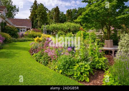 Blick auf abfallenden Garten mit Blumenrabatten. Mit Euonymus undulata 'Emerald'n Gold', Alliums, Heuchera 'Hadspen Blood' und Phuopsis stylos Stockfoto