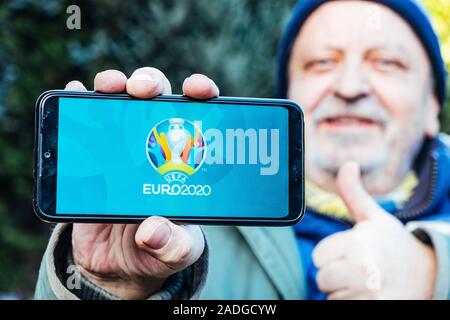 Älterer Mann hält ein Smartphone mit Logo der UEFA Euro 2020 auf dem Bildschirm Stockfoto