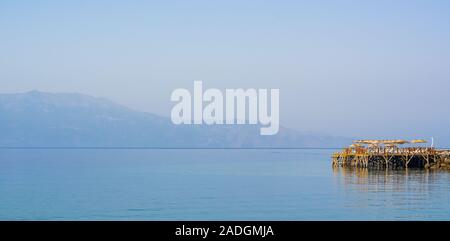 Meer, Pier und Sonnenschirme, Assos, Canakkale, Türkei. Vorbereitung auf die Meeressaison. Fertiger Schreibbereich in Feiertagsgrafiken. Stockfoto