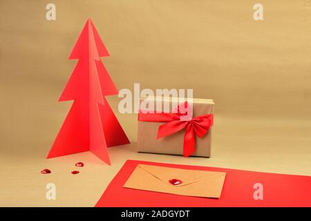 Geschenkbox und Umschlag mit rotem Holz Weihnachtsbaum auf einem natürlichen braunen Hintergrund mit verstreuten Herzen. Stockfoto