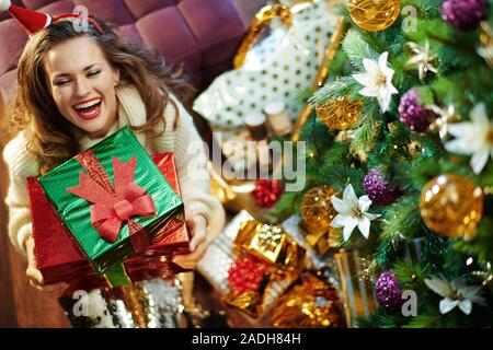 Obere Ansicht von Happy trendy 40 Jahre alte Hausfrau mit langen brünetten Haar in Gold Pailletten Rock und weißen Pullover mit Haufen von Weihnachtsgeschenk Boxen u Stockfoto