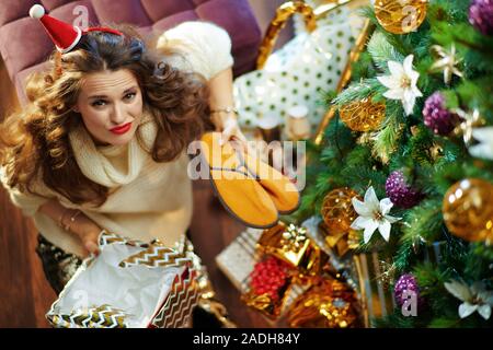 Obere Ansicht von traurig, elegante Frau mit langen brünetten Haar in Gold Pailletten Rock und weißen Pullover unter dem geschmückten Weihnachtsbaum in der Nähe des heutigen Boxen unwra Stockfoto