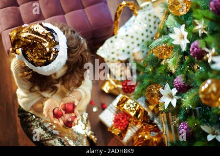 Obere Ansicht von stilvollen Hausfrau mittleren Alters mit langen brünetten Haar in Gold Pailletten Rock und weißen Pullover unter dem geschmückten Weihnachtsbaum in der Nähe des heutigen Stockfoto