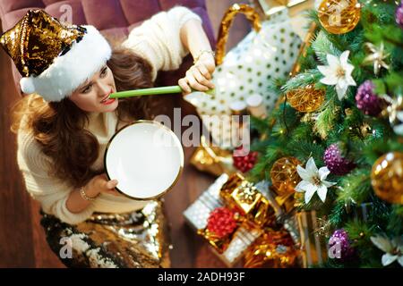 Obere Ansicht von unglücklichen stilvolle Hausfrau mittleren Alters mit langen brünetten Haar in Gold Pailletten Rock und weißen Pullover unter dem geschmückten Weihnachtsbaum in der Nähe von Stockfoto