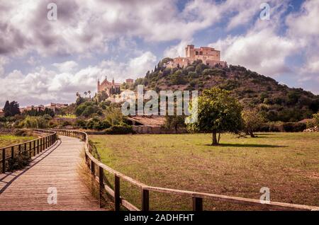 Pfarrkirche und Wallfahrtskirche Sant Salvador in Arta, gelegen auf einem Hügel mit Feldern und einem Holzsteg im Vordergrund, tagsüber mit blauem Himmel Stockfoto