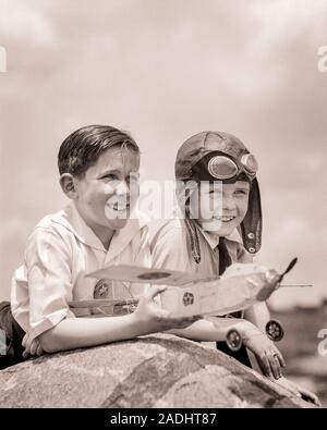 1930er Jahre zwei lächelnde Jungen lehnte sich auf Rock, der ein MODELLFLUGZEUG DER ANDEREN SIE EINE LEDERNE PILOT HELM mit Brille - b11890 HAR 001 HARS ENTSPANNENDE FREUDE FREUDE LIFESTYLE BRÜDER FLUG KOPIE RAUM FREUNDSCHAFT halber Länge INSPIRATION SCHUTZBRILLE MÄNNER GESCHWISTER VERTRAUEN AUSDRÜCKE B&W ERFOLG SKILL AKTIVITÄT UNTERHALTUNG TRÄUME KOPF UND SCHULTERN FRÖHLICHE HOBBY KRAFT SIEG INTERESSE AUFREGUNG HOBBYS WISSEN NIEDRIGEN WINKEL ZEITVERTREIB INNOVATION VERGNÜGEN, EINEN AUF DIE Vorfreude der Geschwister freundlich lächelt KONZEPTIONELLE PHANTASIE FREUDIGE STILVOLLE GUMMIBAND KOOPERATION KREATIVITÄT eifrig Wachstum von Jungfischen Stockfoto