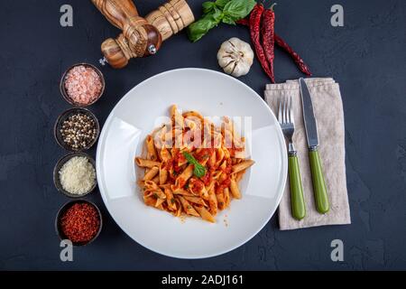 Penne Pasta mit Chili Sauce arrabiata. Klassische italienische Penne Arrabiata mit Basilikum und frisch geriebenem Pecorino auf einem rustikalen Holztisch. Stockfoto
