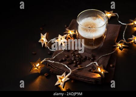 Thermo Glas Tasse Latte Kaffee eingerichteten Weihnachtsbeleuchtung auf dunklen Holztisch. Morgen trinken. Weihnachten und Neujahr Konzept Stockfoto