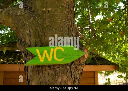 WC wc auf einer hölzernen banner Board auf einen Baum. Einfache handgemachte Design mit Pfeil, der die Richtung der Toiletten. Stockfoto