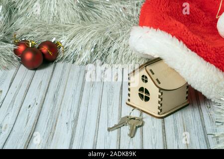 Spielzeug Holz- Haus in Santa Hut und zwei Tasten auf einem Holztisch mit einer Girlande und roten Weihnachtskugeln für Silvester oder Weihnachten dekoriert Stockfoto