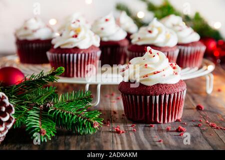 Weihnachten red velvet Cupcakes mit Weihnachtsschmuck, Tanne und Lichtern auf einem rustikalen Holztisch Stockfoto