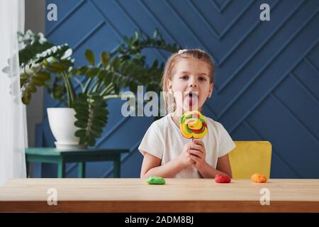 Zeigt Ihre gestaltete Süßigkeit. Kinder spielen mit farbiger Knetmasse auf dem hölzernen Tisch zu Hause Stockfoto